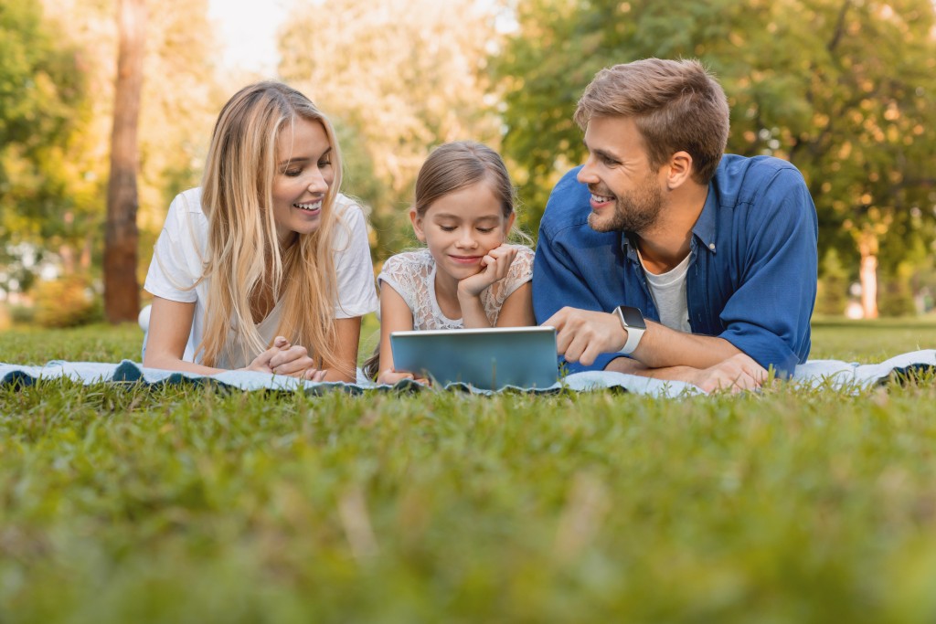 A family smiling while enjoying a picnic in a green park.