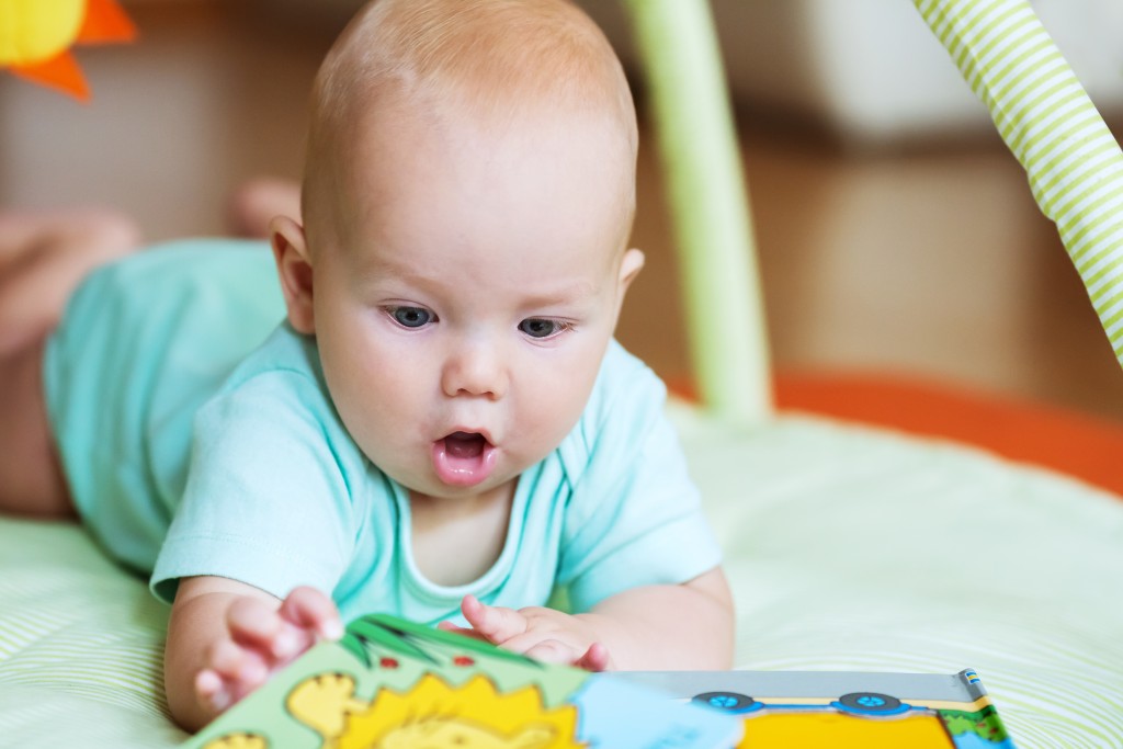 A child is sitting on the floor and reading a book with colorful illustrations.