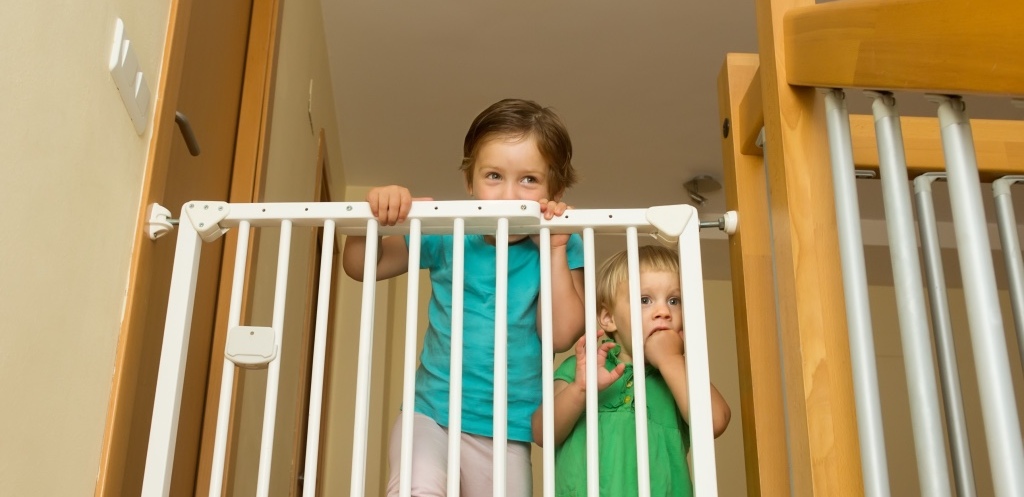 Two little girls approaching safety gate of stairs at home