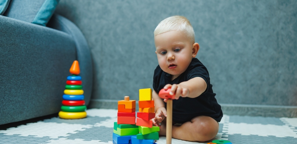 A toddler boy sits on a rug and plays with a wooden pyramid. Development of the baby. Toys for babies