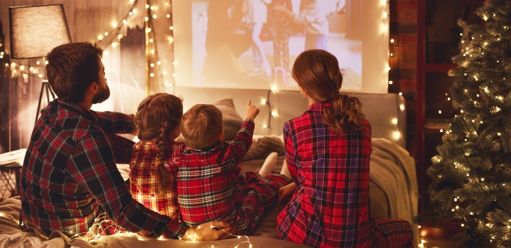 Happy family in checkered pajamas: mother father and children watching projector, film, movies with popcorn in christmas holiday evening at home
